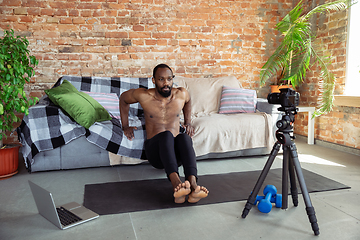 Image showing Young african-american man teaching at home online courses of fitness, aerobic, sporty lifestyle during quarantine, reording on camera, streaming