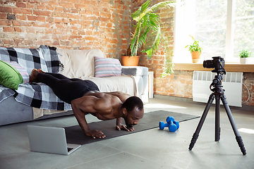 Image showing Young african-american man teaching at home online courses of fitness, aerobic, sporty lifestyle during quarantine, reording on camera, streaming