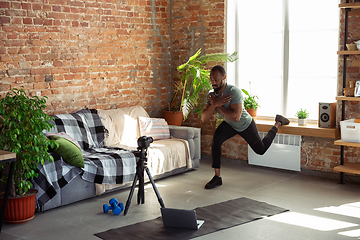 Image showing Young african-american man teaching at home online courses of fitness, aerobic, sporty lifestyle during quarantine, reording on camera, streaming