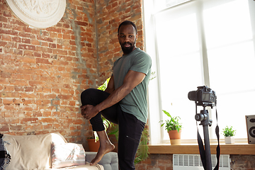 Image showing Young african-american man teaching at home online courses of fitness, aerobic, sporty lifestyle during quarantine, reording on camera, streaming