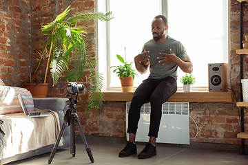 Image showing Young african-american man teaching at home online courses of fitness, aerobic, sporty lifestyle during quarantine, reording on camera, streaming