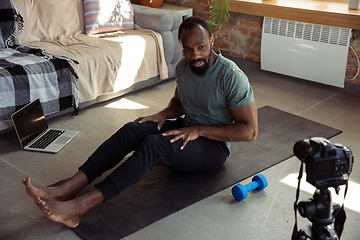 Image showing Young african-american man teaching at home online courses of fitness, aerobic, sporty lifestyle during quarantine, reording on camera, streaming