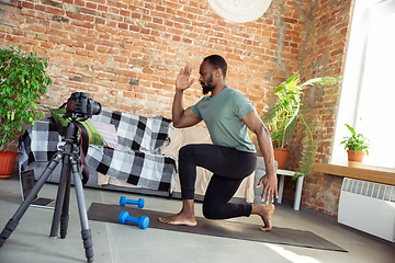 Image showing Young african-american man teaching at home online courses of fitness, aerobic, sporty lifestyle during quarantine, reording on camera, streaming