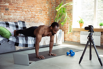 Image showing Young african-american man teaching at home online courses of fitness, aerobic, sporty lifestyle during quarantine, reording on camera, streaming