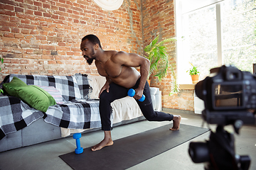 Image showing Young african-american man teaching at home online courses of fitness, aerobic, sporty lifestyle during quarantine, reording on camera, streaming