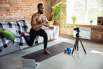 Image showing Young african-american man teaching at home online courses of fitness, aerobic, sporty lifestyle during quarantine, reording on camera, streaming