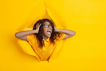 Image showing Cheerful young woman poses in torn yellow paper hole background, emotional and expressive