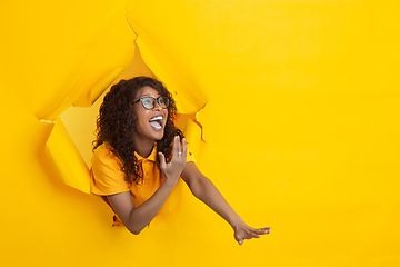 Image showing Cheerful young woman poses in torn yellow paper hole background, emotional and expressive