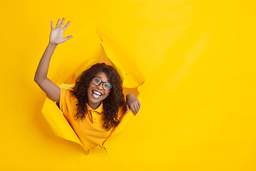 Image showing Cheerful young woman poses in torn yellow paper hole background, emotional and expressive