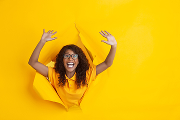 Image showing Cheerful young woman poses in torn yellow paper hole background, emotional and expressive