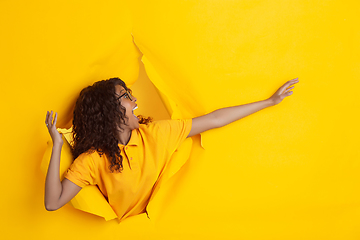 Image showing Cheerful young woman poses in torn yellow paper hole background, emotional and expressive