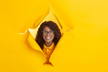 Image showing Cheerful young woman poses in torn yellow paper hole background, emotional and expressive