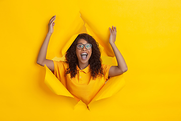 Image showing Cheerful young woman poses in torn yellow paper hole background, emotional and expressive