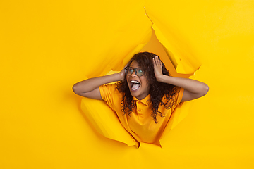 Image showing Cheerful young woman poses in torn yellow paper hole background, emotional and expressive