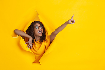 Image showing Cheerful young woman poses in torn yellow paper hole background, emotional and expressive