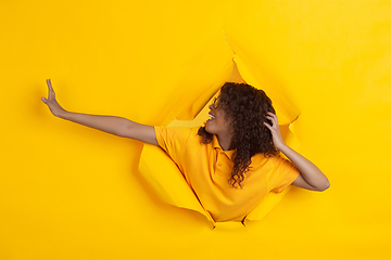 Image showing Cheerful young woman poses in torn yellow paper hole background, emotional and expressive