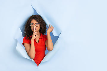 Image showing Cheerful young woman poses in torn blue paper hole background, emotional and expressive