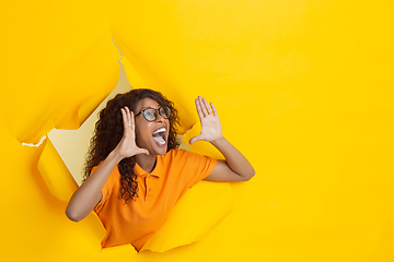 Image showing Cheerful young woman poses in torn yellow paper hole background, emotional and expressive