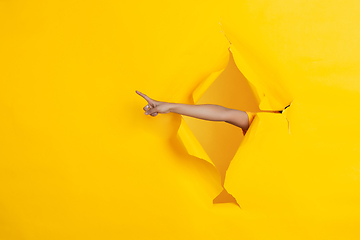 Image showing Female hand pointing in torn yellow paper hole background, celebration