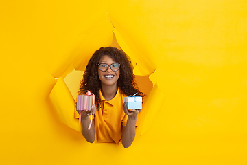 Image showing Cheerful young woman poses in torn yellow paper hole background, emotional and expressive