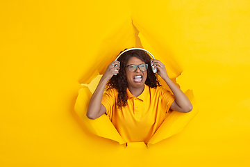 Image showing Cheerful young woman poses in torn yellow paper hole background, emotional and expressive