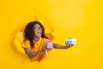 Image showing Cheerful young woman poses in torn yellow paper hole background, emotional and expressive