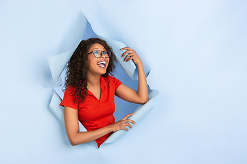 Image showing Cheerful young woman poses in torn blue paper hole background, emotional and expressive