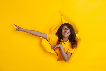 Image showing Cheerful young woman poses in torn yellow paper hole background, emotional and expressive