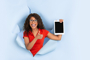 Image showing Cheerful young woman poses in torn blue paper hole background, emotional and expressive