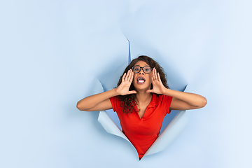 Image showing Cheerful young woman poses in torn blue paper hole background, emotional and expressive