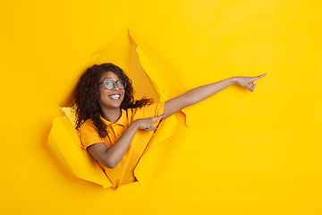 Image showing Cheerful young woman poses in torn yellow paper hole background, emotional and expressive