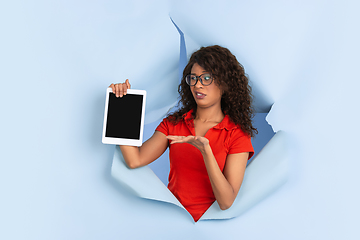 Image showing Cheerful young woman poses in torn blue paper hole background, emotional and expressive