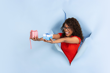 Image showing Cheerful young woman poses in torn blue paper hole background, emotional and expressive