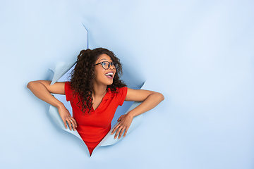 Image showing Cheerful young woman poses in torn blue paper hole background, emotional and expressive