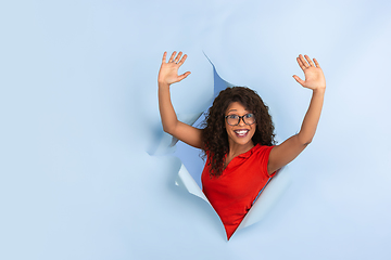 Image showing Cheerful young woman poses in torn blue paper hole background, emotional and expressive