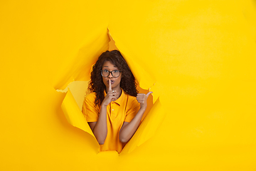 Image showing Cheerful young woman poses in torn yellow paper hole background, emotional and expressive