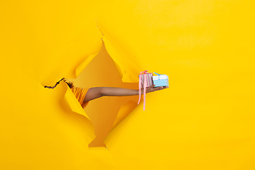 Image showing Female hand giving gift in torn yellow paper hole background, celebration