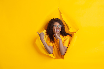 Image showing Cheerful young woman poses in torn yellow paper hole background, emotional and expressive