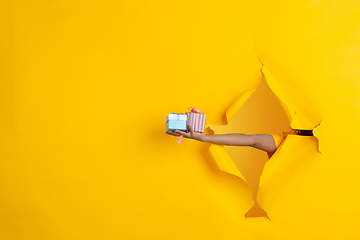 Image showing Female hand giving gift in torn yellow paper hole background, celebration