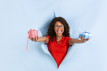 Image showing Cheerful young woman poses in torn blue paper hole background, emotional and expressive