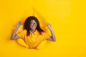 Image showing Cheerful young woman poses in torn yellow paper hole background, emotional and expressive