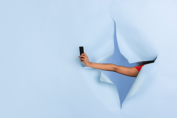 Image showing Female hand giving smartphone in torn blue paper hole background, celebration