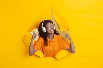 Image showing Cheerful young woman poses in torn yellow paper hole background, emotional and expressive