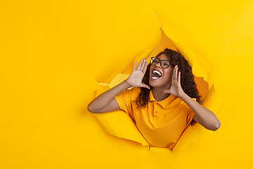 Image showing Cheerful young woman poses in torn yellow paper hole background, emotional and expressive