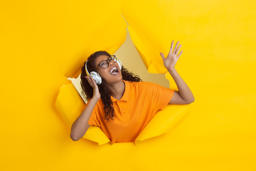 Image showing Cheerful young woman poses in torn yellow paper hole background, emotional and expressive