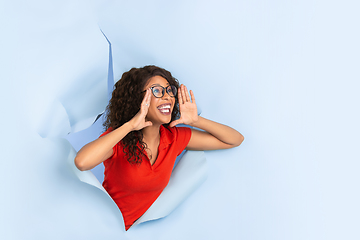 Image showing Cheerful young woman poses in torn blue paper hole background, emotional and expressive