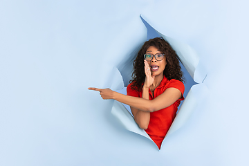 Image showing Cheerful young woman poses in torn blue paper hole background, emotional and expressive