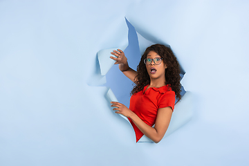 Image showing Cheerful young woman poses in torn blue paper hole background, emotional and expressive