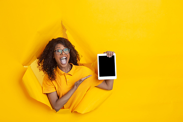 Image showing Cheerful young woman poses in torn yellow paper hole background, emotional and expressive