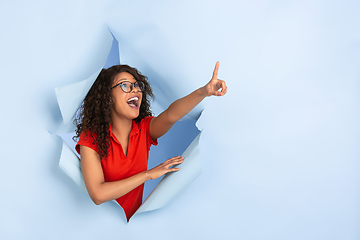 Image showing Cheerful young woman poses in torn blue paper hole background, emotional and expressive